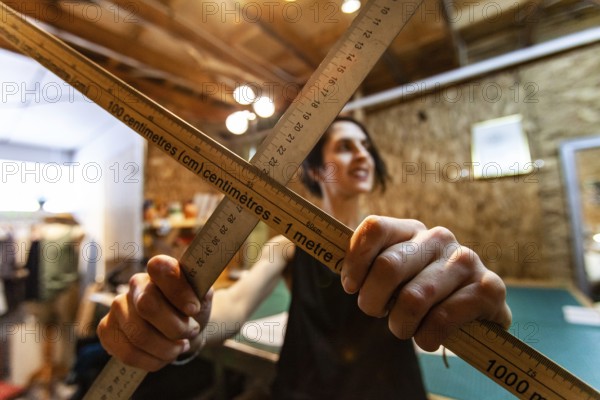 A closeup view of two wood measuring rods being held by a woman tailor inside her retro studio.