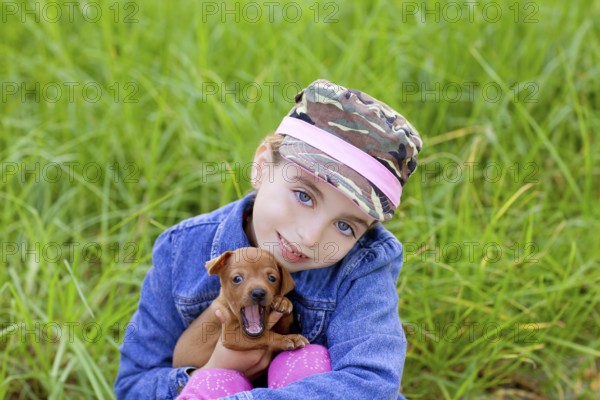Little girl with pet puppy mascot mini pinscher in outdoor green grass