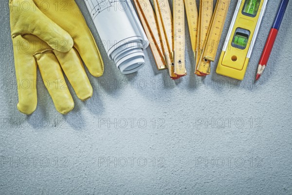 Protective gloves construction level wooden meter blueprints pencil on concrete background building