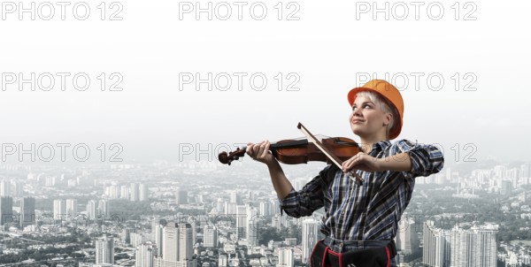 Beautiful young woman in safety helmet playing violin. Smiling professional female builder in