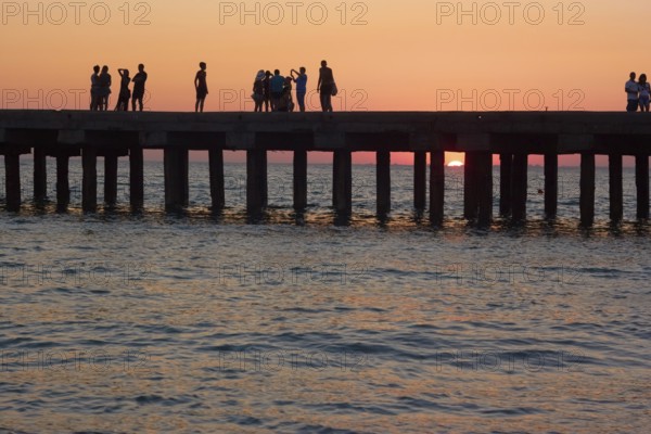 Groups of people on the old pier are photographed and admire the beautiful sunset over the Black