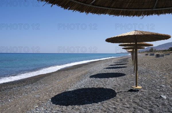 Tropical beach umbrellas providing sunshade for swimmers at an empty beach. Summer vacations.