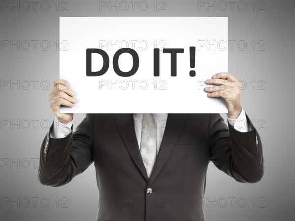 A business man holding a paper in front of his face with the text do it