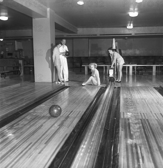 Bowling in the 1950s. A man with three young women in a bowling alley. They are dressed in short
