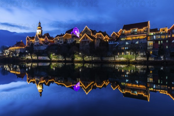 Christmas illuminated house facade of Frohnleiten reflected in the river Mur, blue hour,