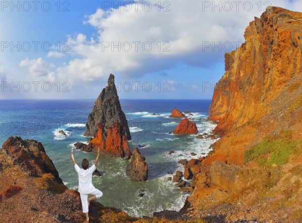 The woman ashore in a white suit for yoga carries out a pose Tree. Atlantic storms. Colorful