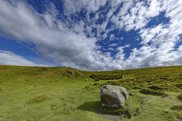 Vast rolling mountain landscape with a cliff and lush green meadows and dramatic skies on the edge
