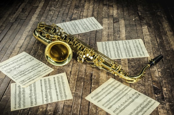 Beautiful yellow saxophone and paper with music score notes lying on a vintage wooden stage