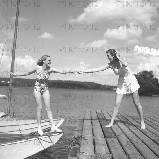 1940s summer. Two young at a marina on a summer's day. The girl getting from the boat onto the