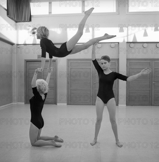 Gymnastics in the 1960s. Three teenage girls are practising gymnastics together in a gymnasium hall