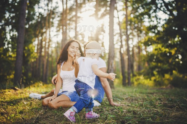 Young parents are taught to walk a daughter of one year on nature in a park on a lawn. The first
