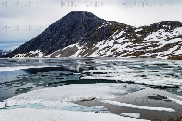 The very cold clear water of the lake Djupvatnet is covered with ice in July. The mountains are
