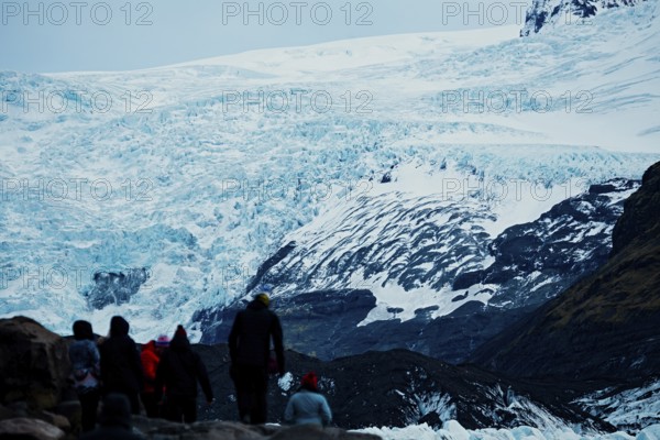 Group of tourists walking towards a large glacier under a cloudy sky, iceberg, glacier, snow, ice