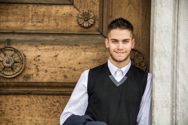 Elegant young man leaning against old wall and wooden door