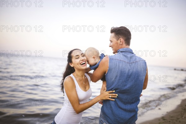 Beautiful young family on holiday with baby. The father holds the blonde girl in her arms, and the