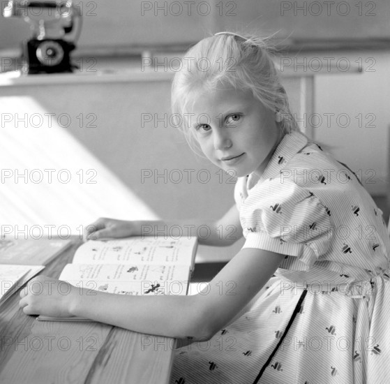 School in the 1950s. A girl is seen sitting at her desk in the classroom reading from the