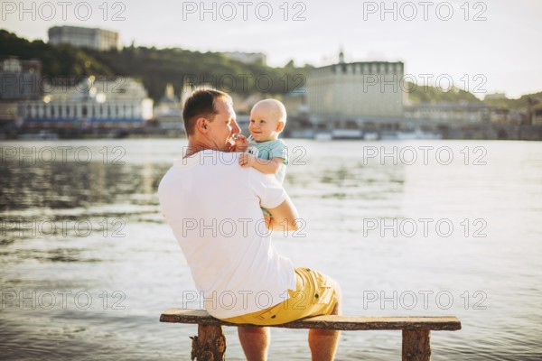 Subject recreation father and little son. Young caucasian dad sits on wooden bench overlooking the