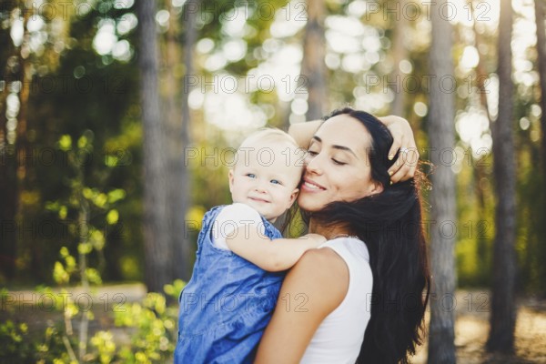 Young beautiful fashionable mother with long brunette hair holding a daughter's blonde with blue