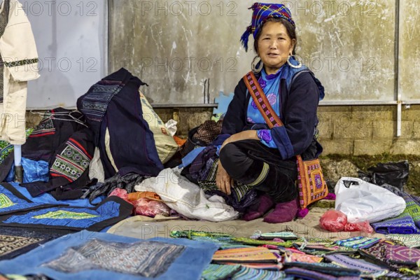 Woman in traditional dress presents handmade textiles at a lively market stall, The street market