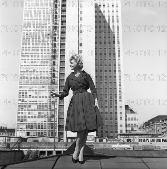 In the 1950s. A woman modelling a 1950s outfit with a jacket and skirt in matching dark. In the