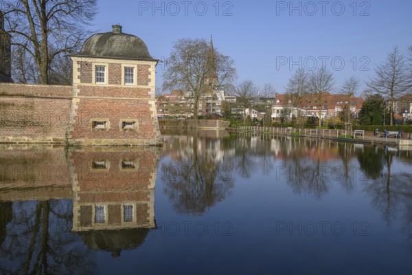 A pavilion at the moat with a clear reflection, surrounded by trees in the park in front of a blue