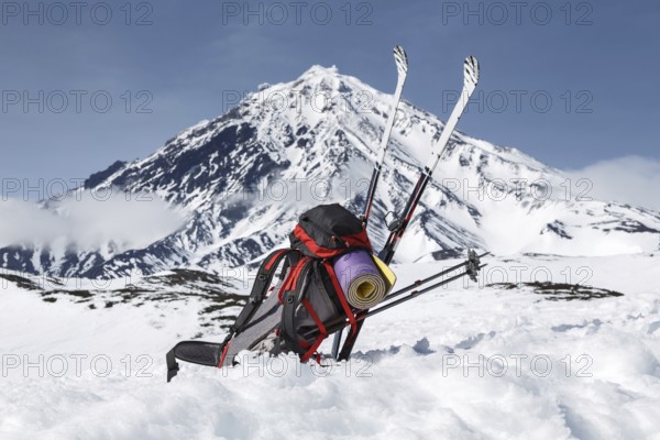 Equipment, backpack, skis and poles lie in snow on background cone of volcano on Kamchatka