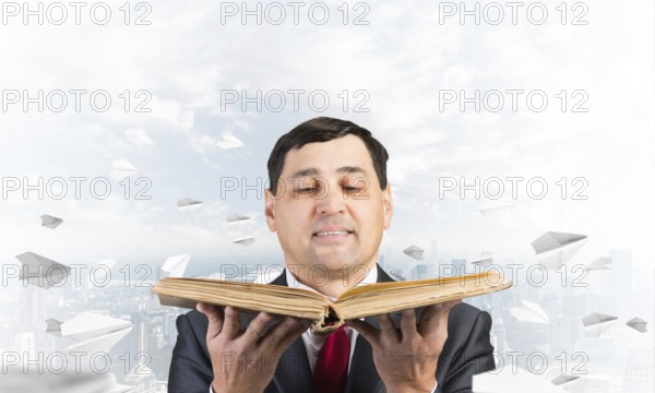 Happy businessman holding open old book. Smiling man in suit standing on downtown background with
