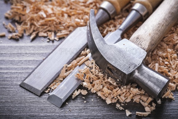 Close up of claw hammer and metal firmer chisels in wooden planning chips on vintage wood board