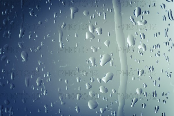 Close up of splashes of water and waterdrops running down on glass panel of bathtub in bathroom