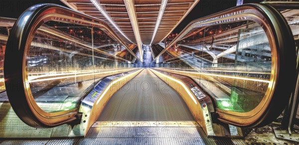 Illuminated escalator, reflected symmetrically in glass walls, Liège-Guillemins railway station,