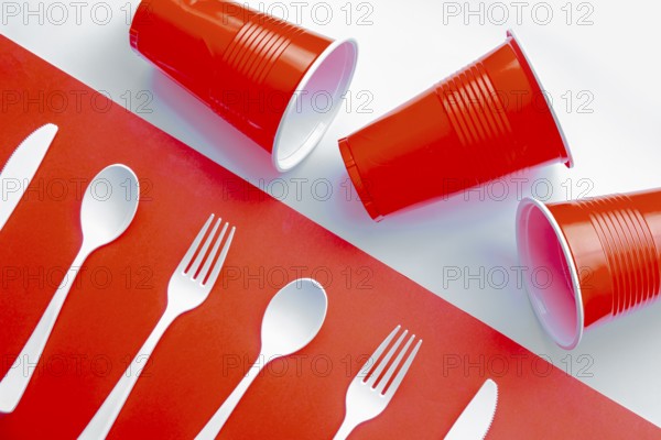 Horizontal view of single use white plastic cutlery and red plastic glass on a red and white