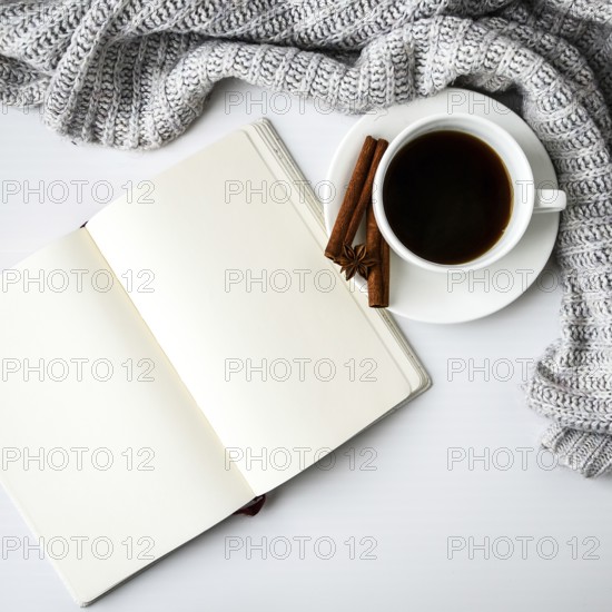 Cup of coffee with notebook cinnamon sticks and anise star on white background. Sweater around.
