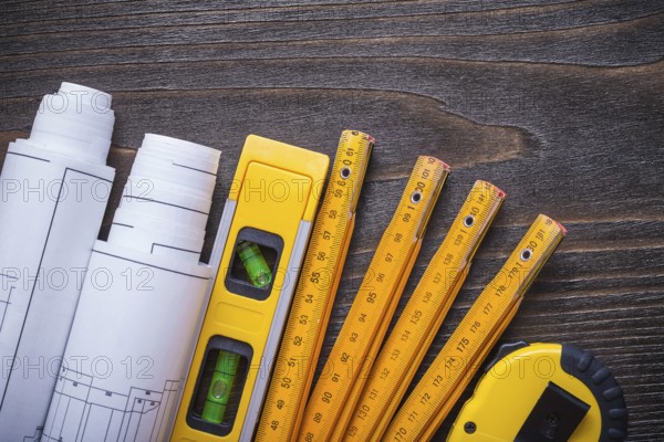 Close up view of blueprint rolls construction level tape-line and wooden meter on vintage wood