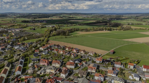 Aerial view of a neighbourhood with numerous houses and surrounding fields under a cloudy sky,