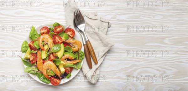 Healthy salad with grilled shrimps, avocado, cherry tomatoes and green leaves on white plate with