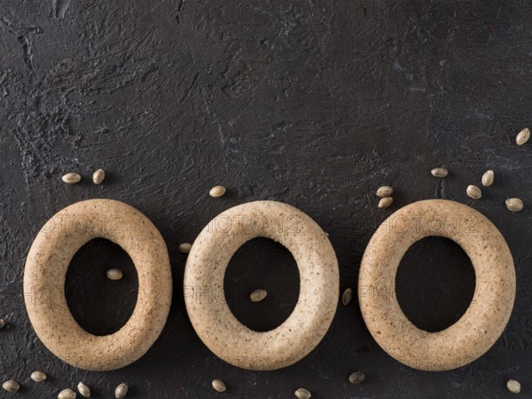 Ring-shaped cracknel with whole grain hemp seed flour and hemp seeds on black background.