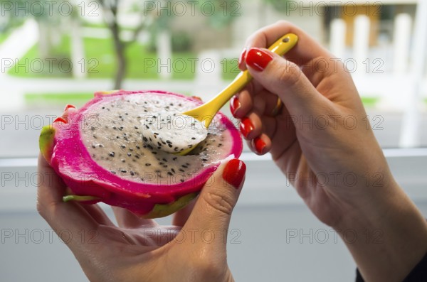 Woman hand eating pitaya with colored spoon