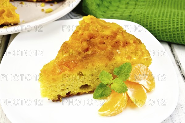 Piece of tart with mandarin, mint, mandarin slices in a white plate, towel on a background of