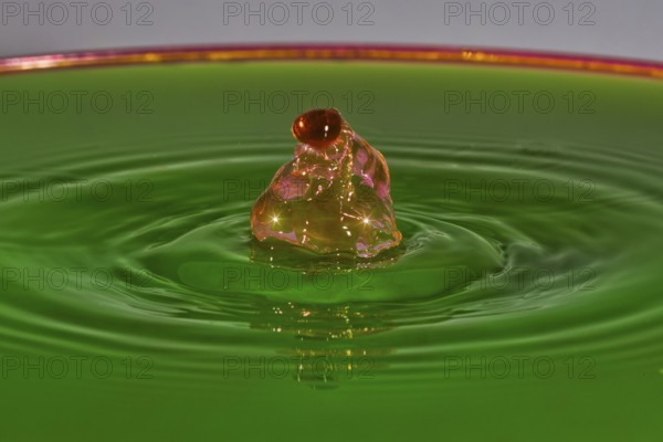 A reddish-brown drop hits green liquid and forms water rings, water droplets, collision, high-speed