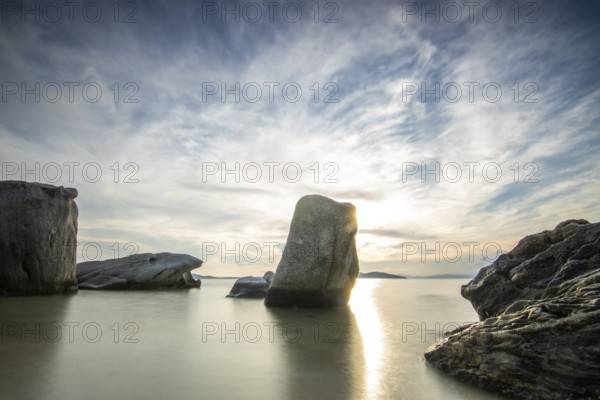 View through rocks on a sandy beach into the sunset. Landscape shot with view to the horizon over