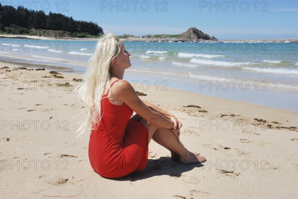 Woman at beach, A woman in a red dress sits on the sandy beach in Erquy, facing the sea under a