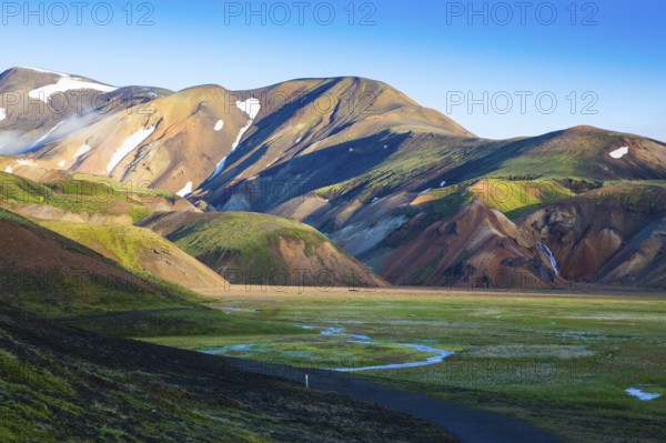Snow lies in the hollows of colorful rhyolite mountains. Green Valley is flooded with melt water.