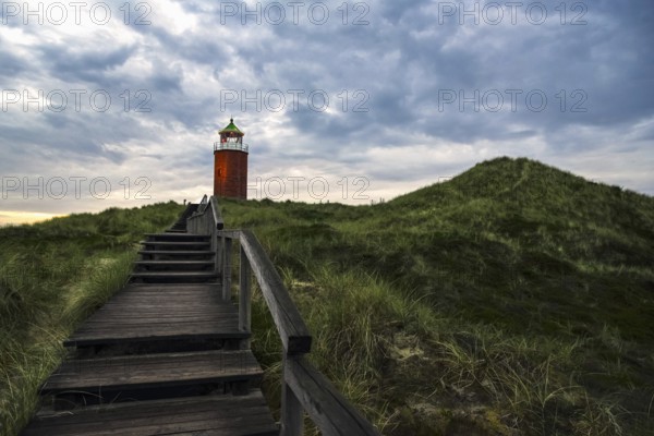 Evening landscape with wooden stairs over marram grass hill, toward red lighthouse, on Sylt island,
