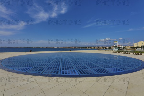 Modern circular solar installation by the sea with clear sky and calm surroundings, artwork