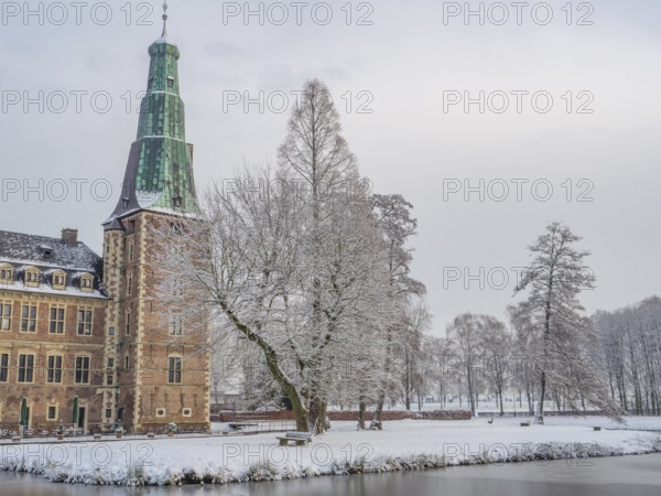 Castle in winter, surrounded by snow-covered trees, with a frozen lake in the foreground, Raesfeld,