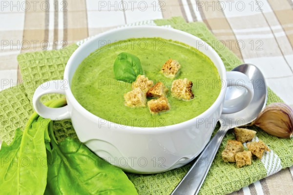 Green soup puree in a white bowl with croutons and spinach leaves, spoon on a napkin on the