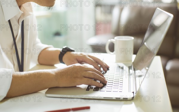 Businessman using laptop with tablet and pen on white table in office with a cup of coffee, side