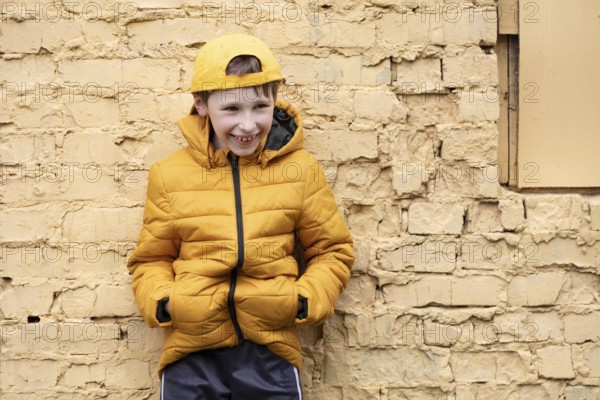 A child on the street A cheerful boy in yellow clothes and a baseball cap stands against a brick