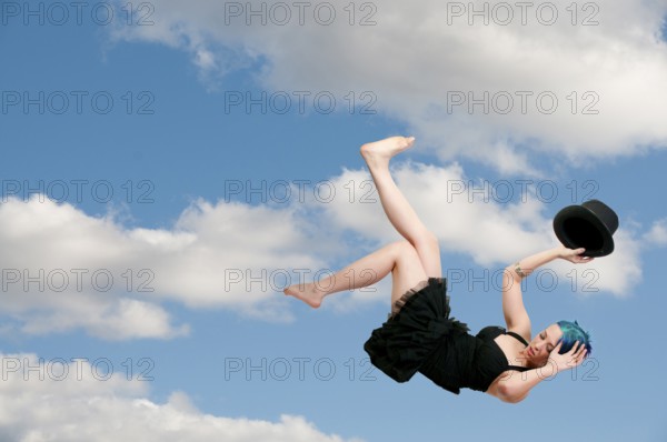 A beautiful young actress dancer wearing a top hat flying through the sky or falling through the