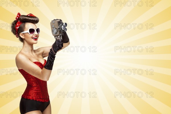 Retro photo of a glamorous pin up girl with an old vintage cinema 8mm camera shooting a film on